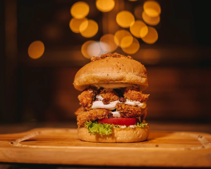 Crispy fried chicken burger on a wooden board with warm lights