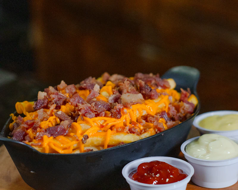 Skillet of fries loaded with cheese and chicken bits with dips